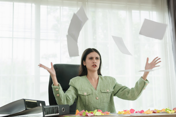 年轻的压力大的女人坐在办公室的办公桌前，带着沮丧的表情撕扯和抛出文件图片下载