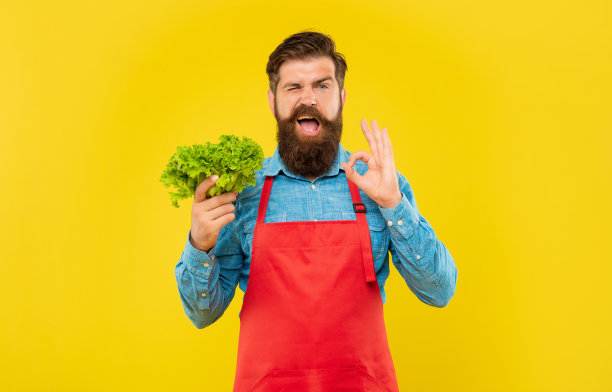 穿着围裙的男子正拿着新鲜的生菜黄底色，菜贩图片下载