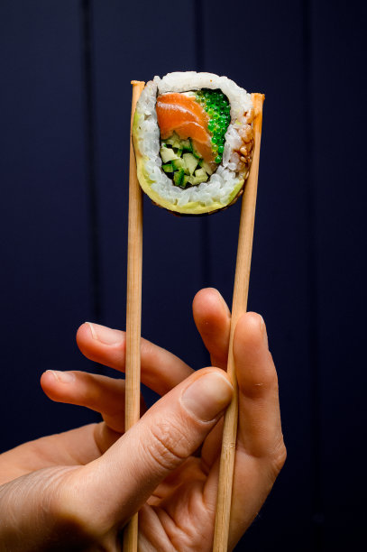 用竹筷夹着一份费城寿司卷，夹着烟熏三文鱼、牛油果、黄瓜和青小牛图片下载