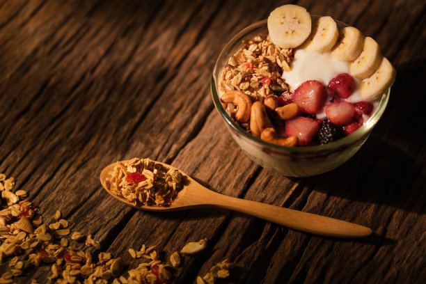 健康的早餐。在阳光照耀下，木桌上放着酸奶、麦片、浆果和香蕉。图片下载
