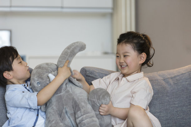 一个小女孩和一个小男孩在客厅的沙发上开心地玩着一个毛绒大象娃娃——照片图片下载