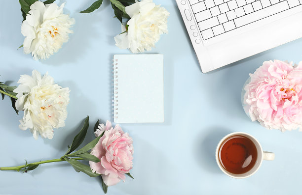 电脑，牡丹花和一杯咖啡放在一张浅色的桌子上。现代女性的桌面，家庭办公室。最小经营理念图片下载