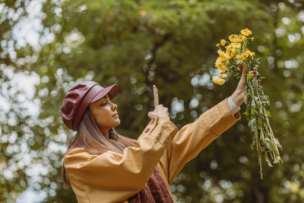 女子在秋天的公园里拍摄一束花图片下载