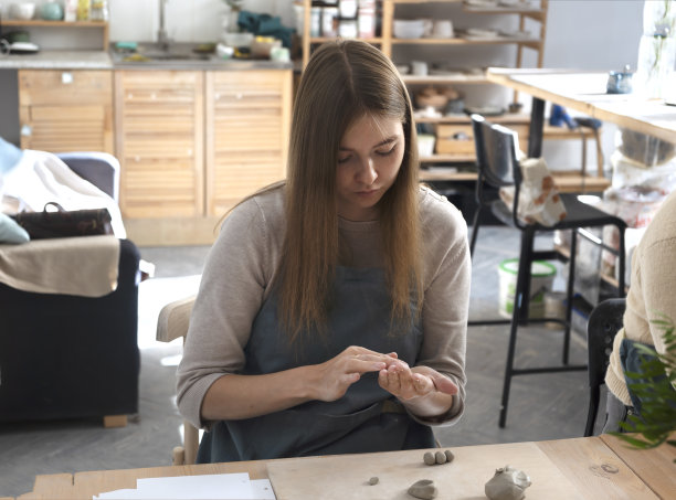 美丽的年轻女子用粘土雕刻了一个马克杯。陶艺工坊班。一个流行的爱好是用生粘土制作陶瓷盘子。图片下载