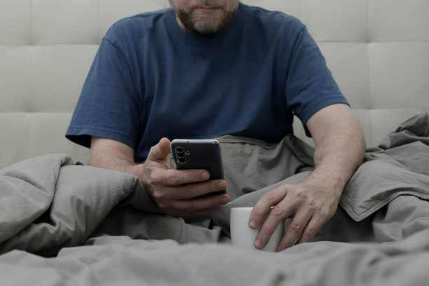 手拿手机，一杯咖啡躺在床上图片下载