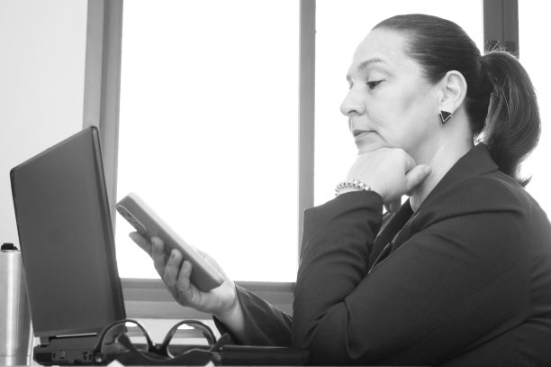 扎着马尾辫的女人，舒服地坐在桌边工作，手里拿着手机和笔记本电脑图片下载