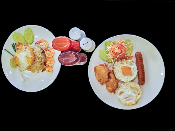食品集。第一套包括煎蛋、香肠和鸡块。第二道菜是虾仁炒饭和煎蛋，配一个酱瓶和一个椒盐瓶。孤立的黑色背景。图片下载