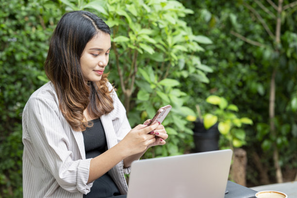 亚洲女商人使用手机和笔记本电脑，桌上放着一杯咖啡图片下载