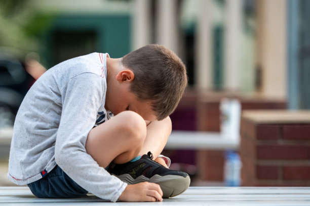 垂头丧气哭泣的小男孩坐在操场上向下看图片下载