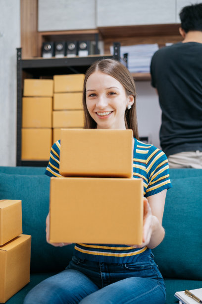 一名女子拿着包裹，看着镜头，站在家里办公室的几个盒子中间。图片下载