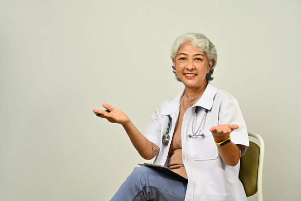 肖像:高级医生穿着白大褂，带着听诊器坐在白色的背景上。医疗保健理念。图片下载