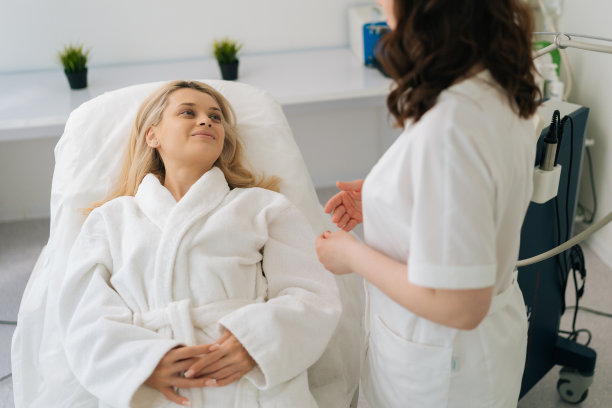 现代美容诊所美容硬件程序前，微笑迷人的金发美女与女美容师交谈的高视角。图片下载