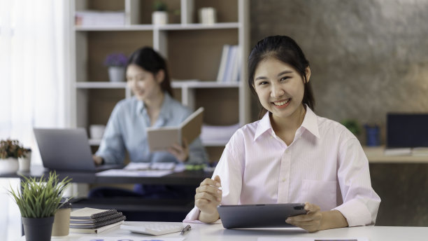 年轻漂亮的亚洲女商人用平板电脑工作，微笑着享受她的工作。图片下载