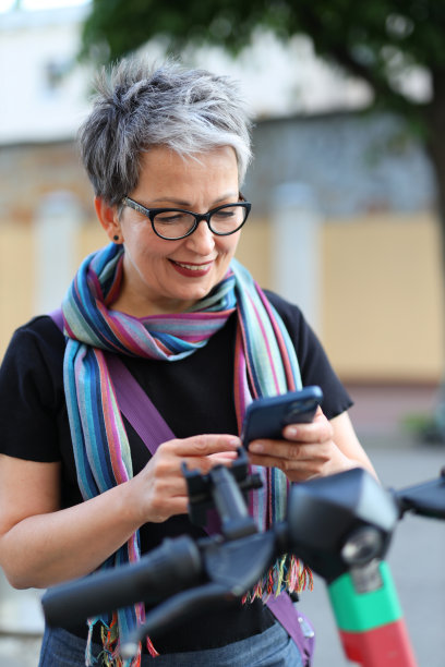 微笑的老妇人使用智能手机和租来的摩托车。图片下载