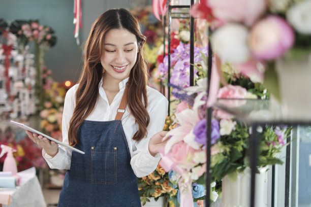 一位美丽的亚洲女花商在美丽的花店里用平板电脑工作。图片下载