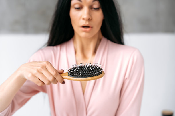 女性手中梳子的特写，梳理后有少量头发脱落，晕眩女性在散焦。保健、美容、脱发问题图片下载