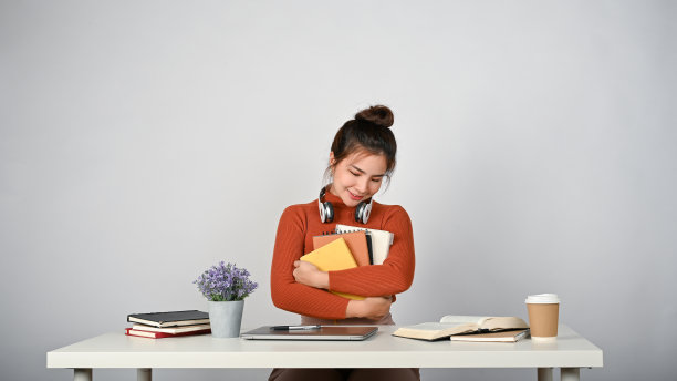 年轻可爱的大学生坐在她的书桌前，白色孤立的背景。图片下载