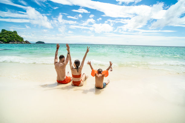 一个幸福的家庭在热带度假的照片，在热带海滩上玩得很开心，玩海水。有父母的小男孩。图片下载