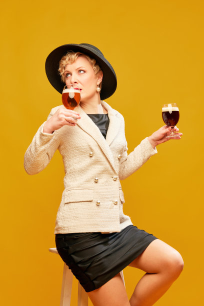 肖像与女士，女人戴着黑色的帽子，拿着不同的啤酒杯，在黄色的背景下愉快地喝酒图片下载