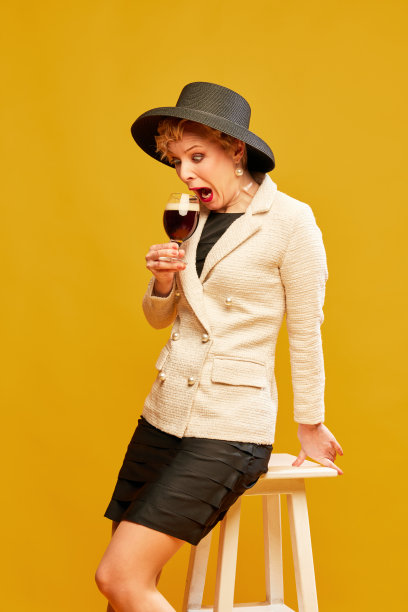 一个穿着复古衣服，戴着帽子，拿着啤酒杯，在黄色背景上大声喊叫的金发成熟女人图片下载