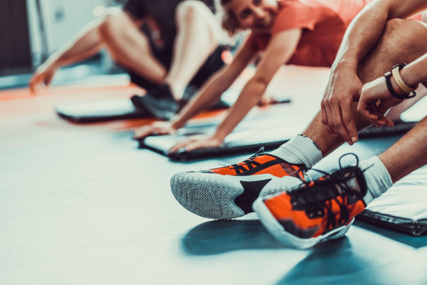 近距离的男子的锻炼运动鞋在前景，三名运动员组在健身房锻炼和伸展，库存照片图片下载