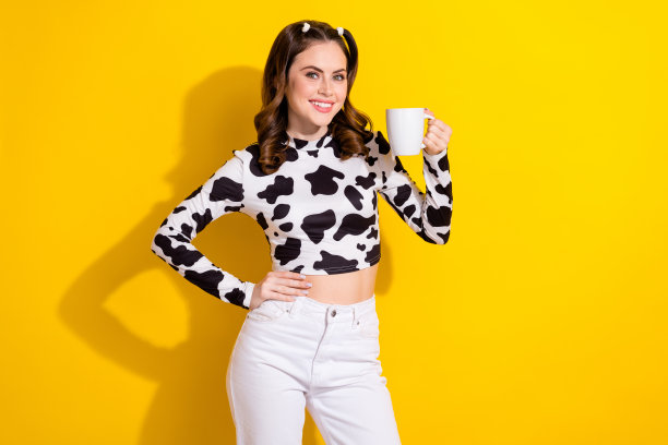照片中可爱可爱的女孩穿着牛皮衬衫喝着热饮，空旷的空间孤立的黄色背景图片下载