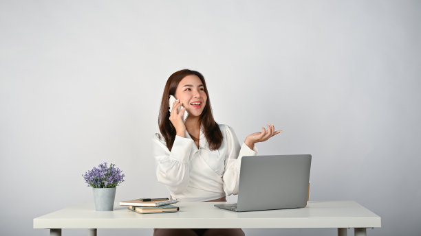 一位快乐的亚洲女商人正坐在办公桌前与她的商业客户通电话。图片下载