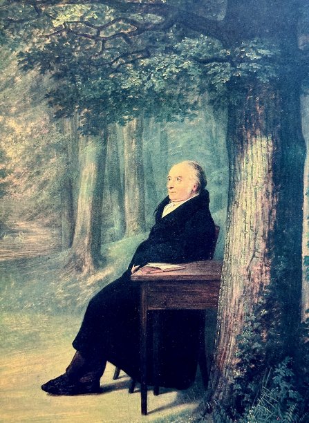 书商穿着黑色正装坐在公园里，他身边的桌子上放着一本书图片下载