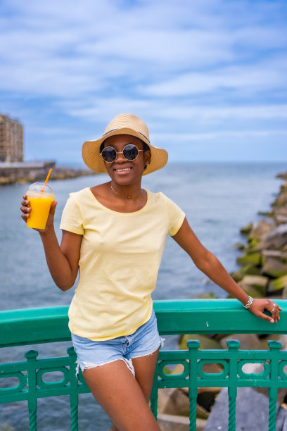 黑人妇女在海边喝橙汁，游客在享受夏天图片下载