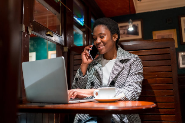 咖啡店里的非洲裔女商人，拿着电脑打电话的金融女性图片下载