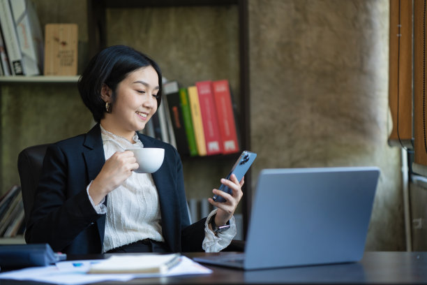 一个漂亮的亚洲女商人坐在她的办公桌前拿着一个咖啡杯。图片下载
