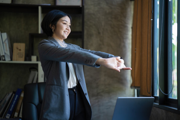 亚洲女商人在办公桌前用笔记本电脑工作时伸展身体放松的照片。图片下载