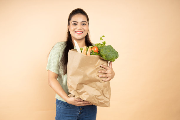 快乐美丽的印度女人拿着装满蔬菜的袋子，站在米色的背景上。特写镜头图片下载