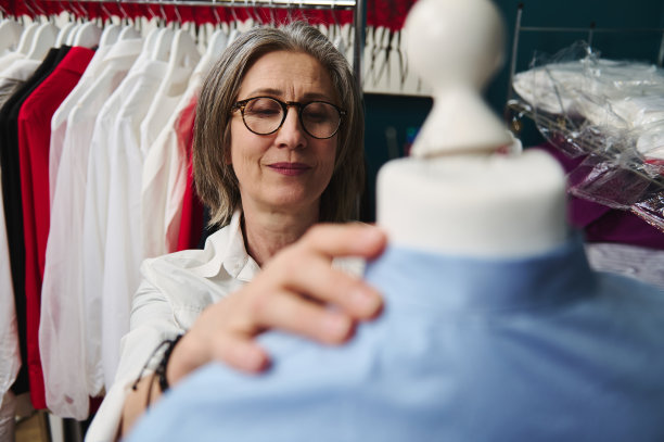 特写愉快的白发白人妇女裁缝在时尚服装设计工作室工作，把一件衬衫从她的豪华新系列上裁剪的人体模型图片下载