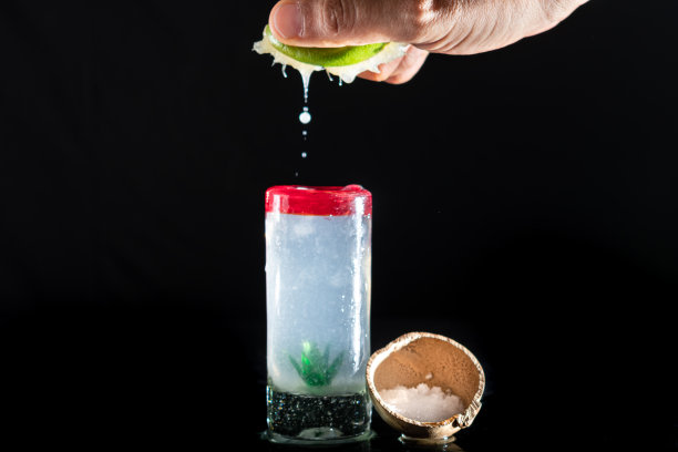 黑色背景的工作室照片。一个人的手把柠檬挤进龙舌兰酒里。龙舌兰酒的内部装饰有一个maguey。旁边有一个盛盐的碗。图片下载
