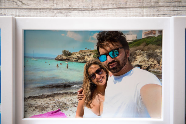 一对情侣在度假时的照片，他们在马洛拉的海滩上旅行。灰色的木质背景。图片下载