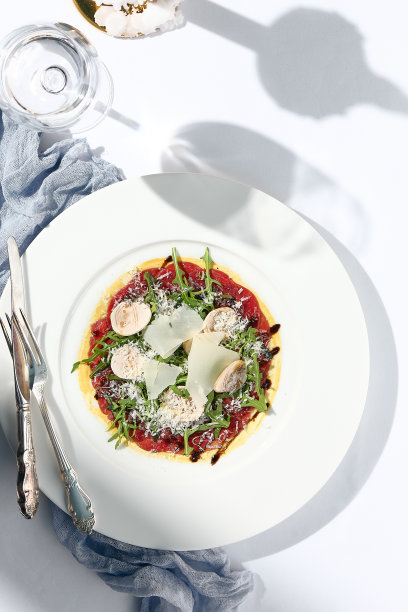 牛肉片配蘑菇和帕尔马干酪。在白色的桌子上简单的现代装饰与牛肉片的幻想晚餐。阳光和严酷的阴影静物。牛肉片开胃菜。图片下载