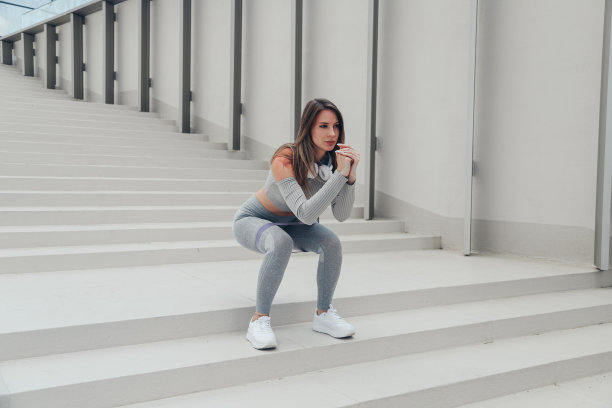 穿着灰色运动服的运动女性在户外用体操松紧带做下蹲仰卧起坐图片下载