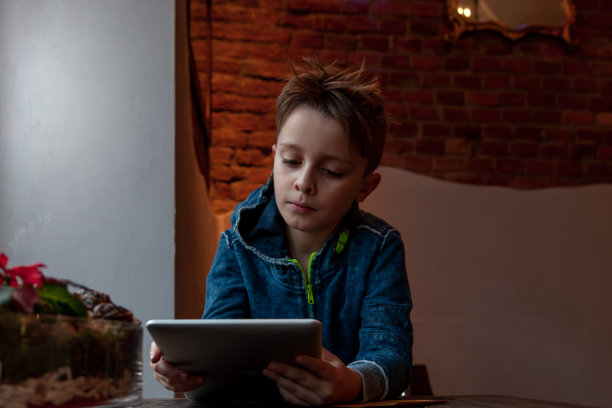 一个小男孩坐在酒吧的大窗户前玩着平板电脑图片下载