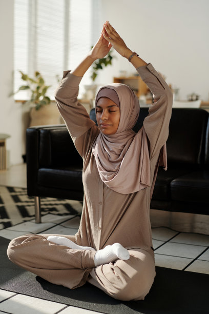 穆斯林妇女坐在莲花的姿势，她的双手放在一起在头上图片下载