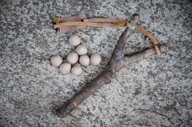 水泥地板上的木制弹弓，上面有粘土球。图片下载