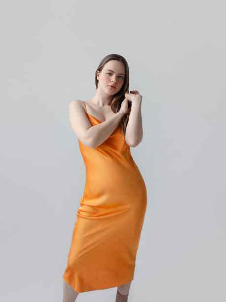 美丽的年轻苗条的女人在优雅的橙色丝绸连衣裙看起来华丽的时装模特工作室肖像在光的背景清新的自然美图片下载