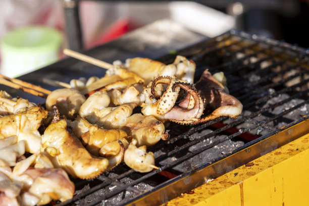 大鱿鱼串在热炉子上烤。傍晚，太阳从侧面照进来。这是一种在泰国很受欢迎的美味街头小吃。有选择性的重点。图片下载