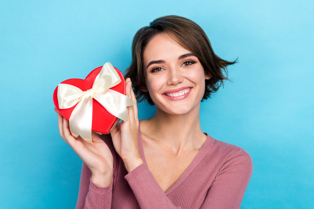 照片迷人的女孩穿着粉红色的衬衫持有心形符号包装礼盒收到惊喜情人节孤立的蓝色背景图片下载