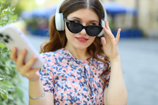 一个小女孩拿着智能手机，戴着耳机享受音乐。图片下载