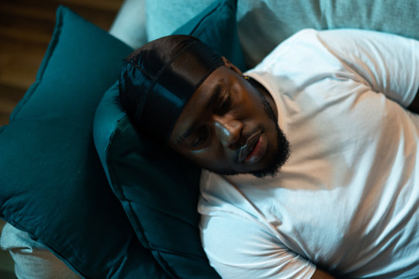 最上面的一张照片是一个男人舒服地躺在沙发上的枕头上。身穿白色t恤、头戴黑色头巾的男孩正在睡觉、休息、小睡图片下载