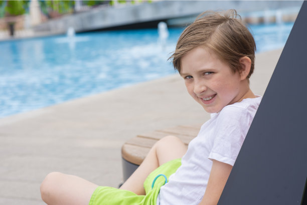 夏天度假时，一个微笑的男孩在酒店泳池前的躺椅上休息图片下载