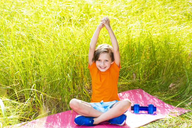 一个小男孩正在室外大自然的垫子或地毯上从事健身、瑜伽、锻炼图片下载