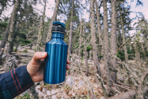 一名男性徒步旅行者手里拿着现代金属旅游水瓶，用来在模糊的森林背景下喝水图片下载