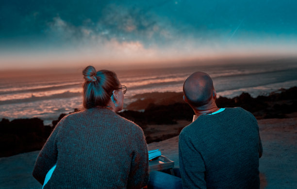 一对白人异性恋夫妇坐在一起看海洋上的星空图片下载
